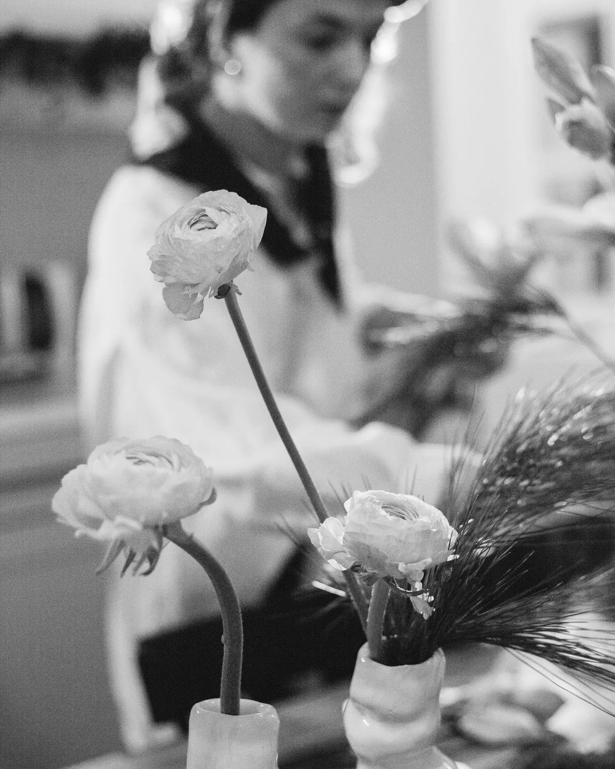 En florist i basker arrangerar vita ranunkler i en rundad vas, i svartvitt